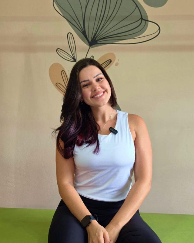 Yasmin sentada no consultório, de regata branca, sorrindo